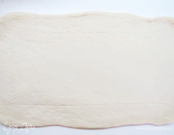 Большую часть раскатываем в широкий и длинный пласт. Длина пласта должна быть равна ширине вашего противня. Ширина будет немного меньше, примерно 20 см на длину пирога + 5 см с каждой стороны на подгиб теста.
Аккуратно тупой стороной ножа на раскатанном пласте теста очертить прямоугольник (область выкладывания начинки), отступая от каждого края примерно 5 см. 