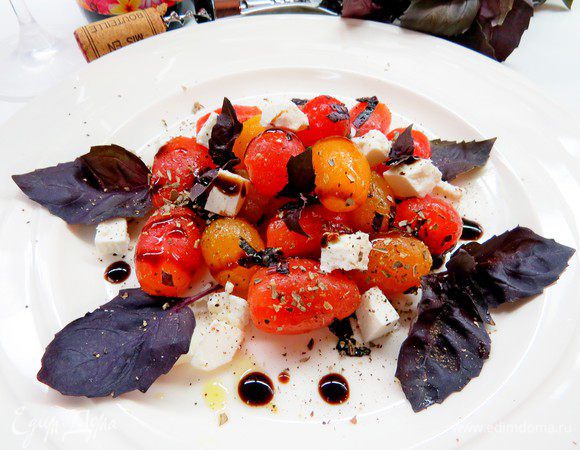 В емкости для салата приправить помидоры сухими итальянскими травами (состав выбирайте на свой вкус), черным перцем, уксусом, оливковым маслом, базиликом, добавить кубики феты. Дать охладиться и настояться в холодильнике не менее 30 минут. При необходимости перед подачей приправить солью.