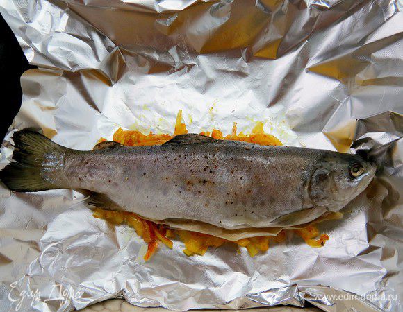 Противень застилаем пергаментом, а потом фольгой (для лучшей термоизоляции). Также из фольги делаем лодочки для каждой рыбки. В каждую лодочку выкладываем лук. Сверху — форель, распластав оную на животе. Закрываем лодочки, стараясь это сделать так, чтобы фольга не касалась шкурки рыбы. Отправляем в духовку при 180-200°C на 20–25 минут. 