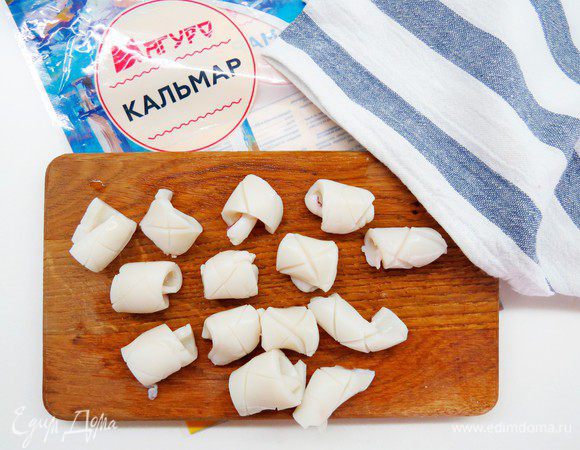 Опустить подготовленнные кусочки кальмара в кипяток секунд на 30, вынуть и тут же остудить в холодной воде, после чего кальмаровые пластины свернутся в трубочки надрезами наружу и станут похожими на шишки.