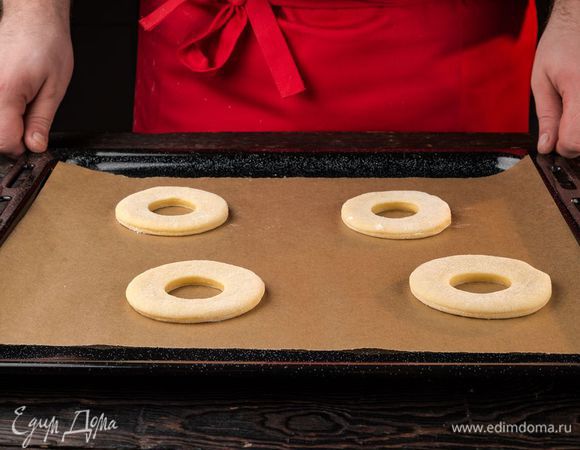Раскатайте тесто в пласт толщиной около 1 см. Вырежьте стаканом или бокалом кружки, а рюмкой внутри маленькие кружки. Выложите пончики на противень для расстойки.
