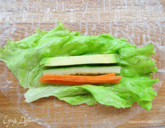 Один рисовый блинчик кладем на разделочную доску, наливаем на него 2 столовые ложки воды, распределяем воду руками по всему блинчику, он смягчится. 
В центр кладем лист салата, на него — полоски моркови, огурца и авокадо в произвольном порядке. 