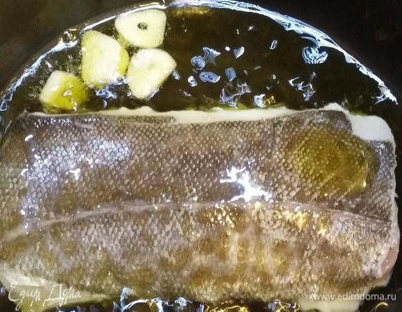 Убавляем огонь (2 из 10), даем маслу остыть несколько минут и выкладываем шкуркой верх кусочки рыбки. Масло должно окутывать рыбку, треска должна тушиться, но не жариться! Видны небольшие пузырьки. Операция похожа на поширование. Держим рыбу 7 минут, шевеля сотейником, чтобы масло покрывало кусочки сверху. Выключаем плиту, переворачиваем рыбу и готовим еще 2 минуты.