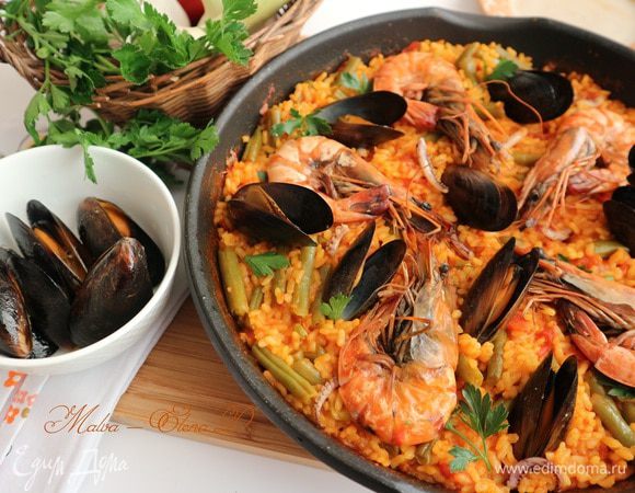 За 1-2 минуты до полной готовности риса с овощами поместить в сковороду морепродукты: креветки, щупальца кальмара, мидии, накрыть крышкой. Выключить огонь, перед подачей дать постоять минут 5. Украсить зеленью петрушки.