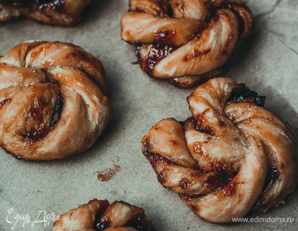 Обомните тесто и раскатайте в прямоугольный пласт толщиной 0,5 см. Смажьте половину теста джемом (я использовала сливовое варенье), сложите тесто пополам, накрывая смазанную часть несмазанной. Надрежьте тесто от места сгиба к краю, чтобы у вас получились полосы теста шириной 1,5 см. Возьмите полоску за край со сгибом и край с двумя концами и начинайте поворачивать их в разные стороны, создавая спираль. Следуя этим движениям по кругу, соберите булочку, как на фото.