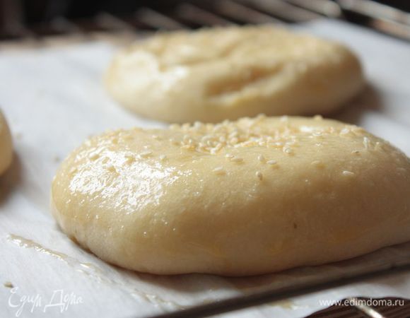 После чего выложите сформованные булочки получившимся швом вниз на теплый противень, накройте их полотенцем и оставьте еще на полчаса. Противень можно предварительно смазать сливочным маслом или выстелить пекарской бумагой.
Расстоявшиеся булочки смажьте взбитым яйцом и посыпьте кунжутом.