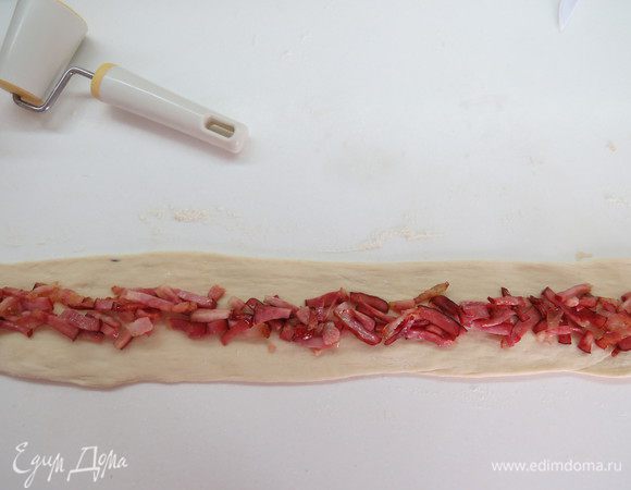 Первую часть тесто скрутить в длинную колбаску и раскатать в полосу длиной примерно 60-70 см, шириной 8 см.
В середину раскатанной полосы выложить нарезанную колбасу, сложить боковые стороны внахлест и хорошо защипать сверху по шву. Получится длинная колбаска из теста с начинкой.
Тот же процесс повторить для двух оставшихся полосок теста, одну наполняем нарезанными маслинами, другую тертым сыром.