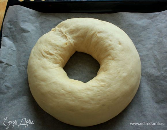 Перенесите его на застеленный пергаментом противень и сформируйте венок. Внешний (верхний) край скрученного пласта должен быть снаружи и доходить почти до пергамента. Тщательно закрепите концы рулета вместе.