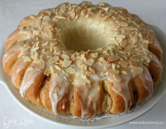 Разогрейте духовку до 200°С. Выпекайте венок 25-30 минут до золотистого цвета. Выньте из духовки и полностью остудите на решетке. Уменьшите температуру в духовке до 170°С. Противень застелите пергаментом и распределите на нем миндаль. Обжаривайте в течение 6-8 минут до легкого золотистого цвета. Смешайте сахарную пудру с лимонным соком и кистью, нанесите помадку на венок. Сразу же посыпьте поджаренным миндалем.