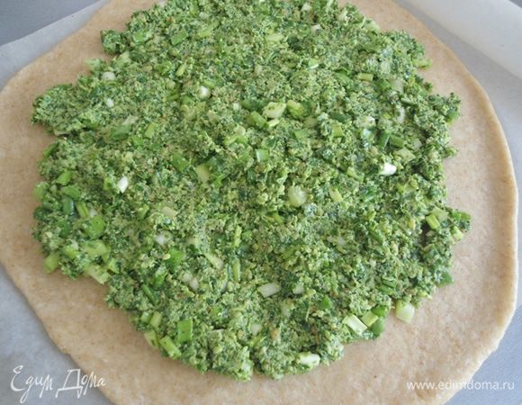 Тесто раскатать на бумаге для выпечки в круг. Зеленую и ароматную начинку распределить по тесту, оставляя края свободными.