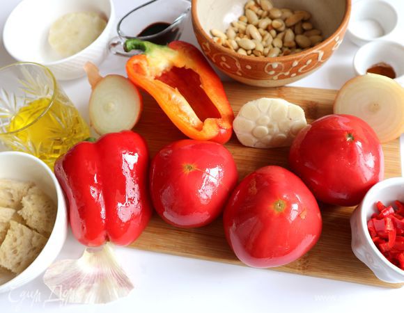 Перец чили порезать на кусочки. Одну половинку чеснока поместить на противень срезом вниз, предварительно смазав чеснок кисточкой оливковым маслом. Также смазать красный сладкий перец (порезать пополам вдоль, вынуть семенную часть, хвостик оставить), помидоры, лук с нижним слоем шелухи, разрезанный поперек. Поместить на противень овощи и запекать их в духовке примерно 30 минут. Запечь кусочки хлеба, порезанного на крупные кубики, в течение 10 минут, смазав их предварительно оливковым маслом.