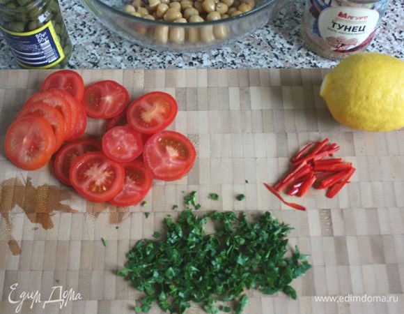 Мясо тунца вынуть из банки в большую миску и размять на средние кусочки. Слить жидкость из банки с нутом и промыть его холодной водой. Промыть нужное количество каперсов. Помидоры помыть, нарезать половинками или кружочками. Петрушку и чили мелко нарезать. Если любите острую пищу, то чили можно нарезать, не вынимая семена. Петрушки нужен большой пучок, чили на ваш вкус, можно и без него.