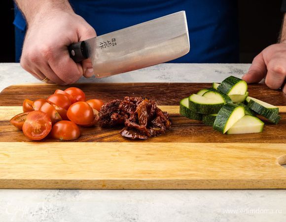 Нарежьте овощи: цукини — крупными ломтиками, свежие и вяленые помидоры нарежьте пополам.