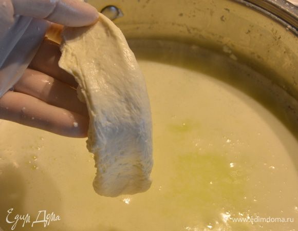 Теперь масса очень хорошо расплавилась, стала эластичной и ее можно растягивать. Нужно несколько раз вытянуть и сложить сырную массу, чтобы не осталось крупинок творога и кусочек моцареллы был слоистым. Все это время периодически опускаем сырную массу в горячую сыворотку, чтобы можно было ее растянуть.