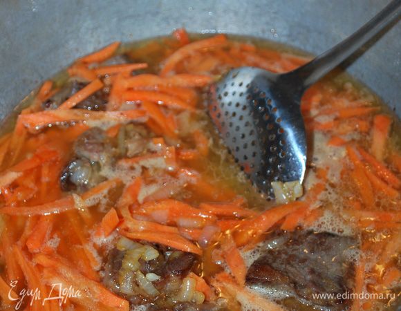 Наливаем кипяток, это все вместе называется зирвак — это основа для плова. Солим сильнее, но не сильно пересаливаем. Добавляем чеснок в головках и половину зиры. Варим, чтобы морковь стала полумягкой, но не сильно перевариваем.