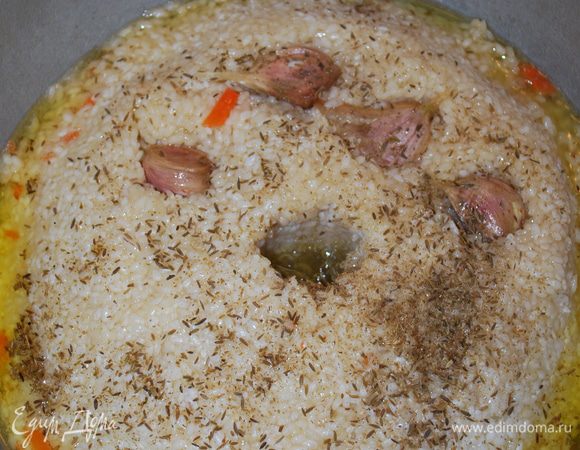 Посыпаем сверху риса оставшуюся зиру и кладем чеснок. Делаем в середине риса углубление до дна, чтобы выходил пар, убавляем огонь и закрываем крышкой. Варим 40 минут. Пробуем на готовность рис. Выключаем огонь. Даем плову постоять, отдохнуть минут 10.