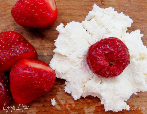 Смоченными в холодной воде руками из творожной массы формируем небольшие лепешечки, внутрь кладем ягодку и заворачиваем ее в творожною массу, делаем небольшие шарики.
