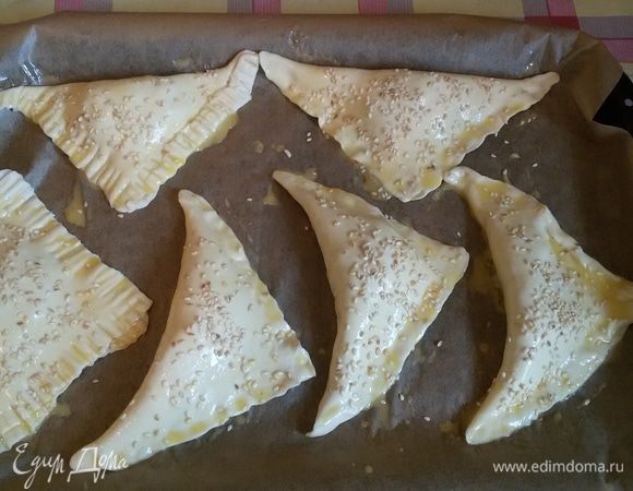 Далее формируем треугольнички и хорошо слепляем края, чтобы сыр не вытек во время приготовления. В разогретую духовку до 180°С на 15-20 минут ставим противень с нашими треугольничками, которые я уже смазала взбитым яйцом и посыпала семенами кунжута.