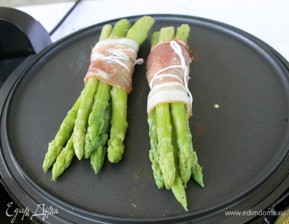 Спаржу посолите, поперчите и добавьте оливковое масло. Соберите в пучки по 6 штук, обмотайте полосками бекона, закрепите кулинарной нитью и оставьте на 15 минут.
