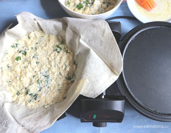 Растопить сливочное масло, охладить до теплого состояния, смешать с йогуртом, смазать кисточкой лист лаваша маслом с йогуртом, положить часть начинки, разровнять. 