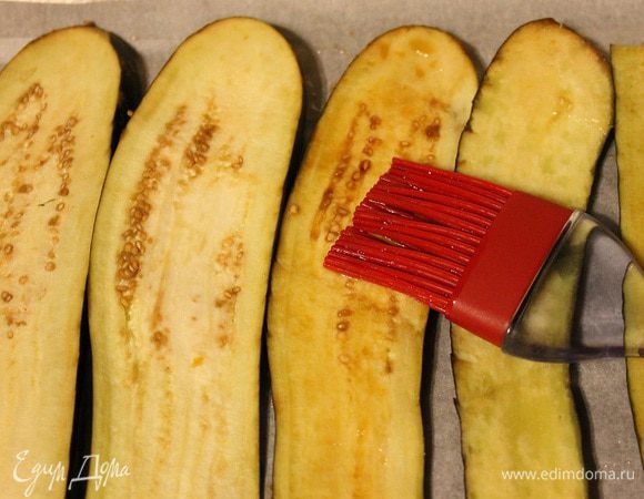 Баклажаны понадобятся большие и длинные, нарезать их пластинами 3–5 мм, смазать с двух сторон маслом и соевым соусом, выложить на противень, застеленный пергаментом. Запекать при температуре 180°C 10–15 минут. Остудить.