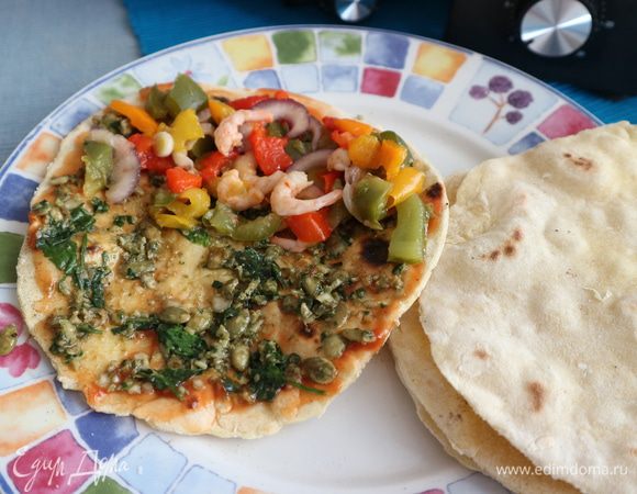 Сразу после приготовления (иначе лепешка не будет эластичной, а будет ломаться) всю поверхность лепешки смазать острым томатным соусом (кетчупом). Затем всю поверхность смазать песто (тыквенные семечки, нарезанный базилик и петрушка, очищенный и нарезанный чеснок, кусочки очищенного от семян красного острого перца, нарезанные оливки смешать с остальными ингредиентами песто, вместо воды, указанной в ингредиентах, лучше взять жидкость от консервированных оливок, просто я не нашла ее в запрашиваемом перечне. Все измельчить в блендере). Начинку следует положить на половинку лепешки. Приготовление начинки в следующем шаге.