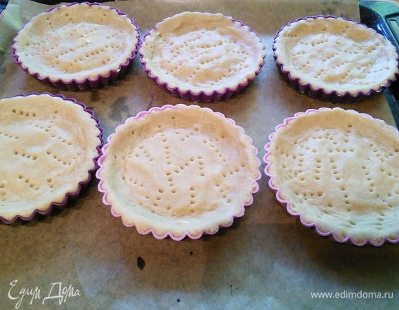 Тесто разделить на 8 частей (количество тарталеток зависит от величины ваших формочек). Выложить тестом формочки и вилкой сделать дырочки. У меня силиконовые, поэтому я их не смазывала маслом, но если у вас другие, то это нужно сделать обязательно + посыпать мукой. Тесто очень нежное и крохкое, так будет легче его извлечь. 