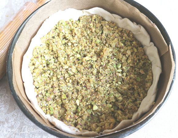 Форму (дно и борта) застелить пекарской бумагой. Поместить больший круг теста на дно разъемной формы, сверху — слой начинки.