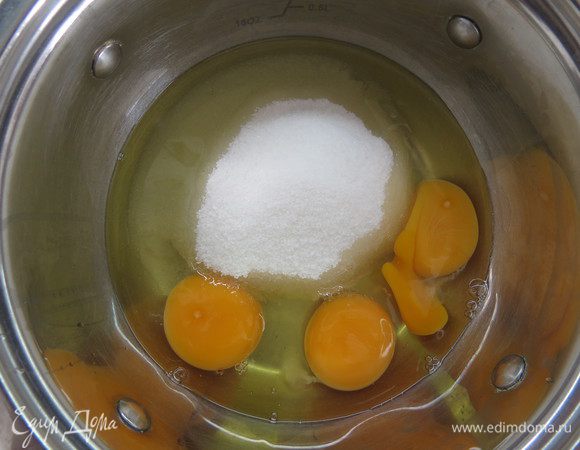 Готовим заварной бисквит Женуаз. Организуем водяную баню: в одну кастрюльку наливаем воду и ставим на огонь, на эту кастрюльку водружаем вторую. Кипящая вода в первой кастрюльке не должна касаться дна второй кастрюли. Во вторую кастрюльку помещаем 3 яйца и сахар. Взбиваем яичную смесь на малой скорости миксера до полного растворения сахара.
