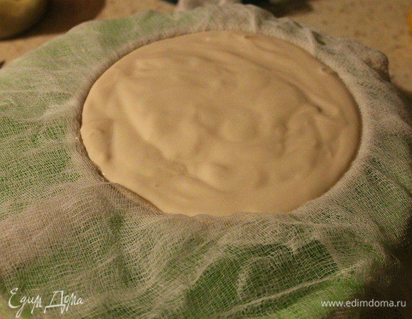 В глубокую миску поставить сито, сверху положить марлю, сложенную в 4-5 слоев. Налить ряженку, завернуть края марли и убрать в холодильник на ночь.
