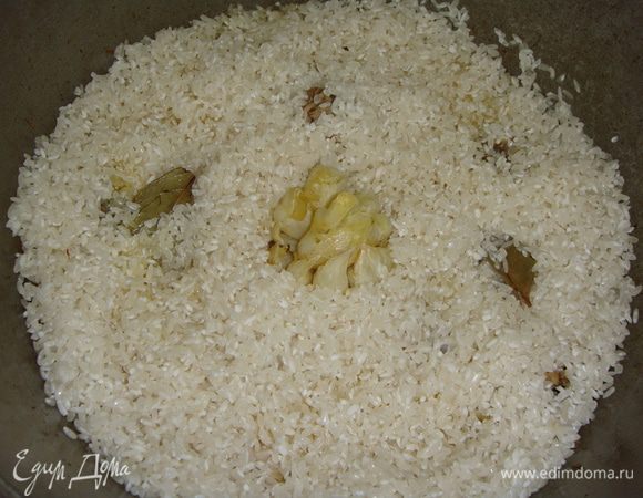 Чеснок вынуть, положить вымытый лавровый лист. Выложить в казан рис, в середину вдавить чеснок.