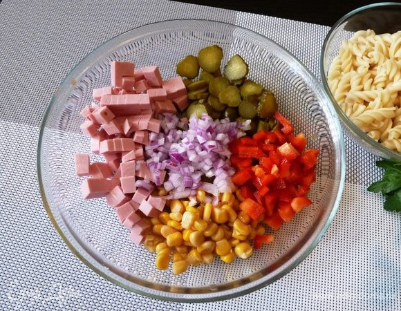 Колбасу и сладкий перец режем кубиком, маленькие маринованные огурчики (пикули) колечками. Если лук острый, то его стоит залить горячей водой на полминутки, чтобы ушла горечь. А если лук сладкий, то его просто мелко нарезать. Добавить консервированной кукурузы.