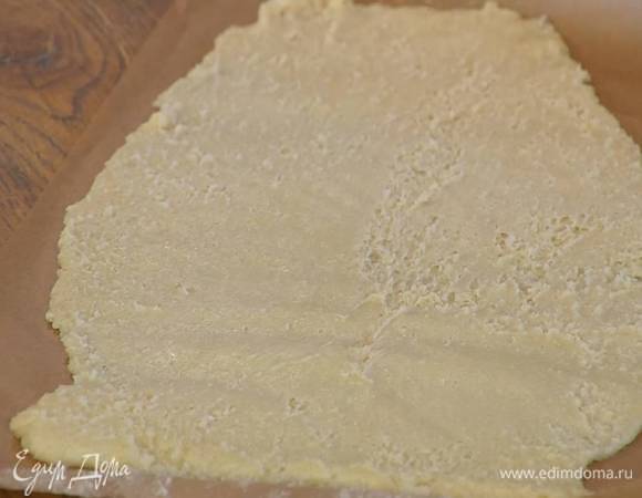 Поместить тесто между двумя листами бумаги для выпечки и раскатать в тонкий пласт, затем верхний слой бумаги снять и выпекать корж в разогретой до 190°С духовке до золотистого цвета.