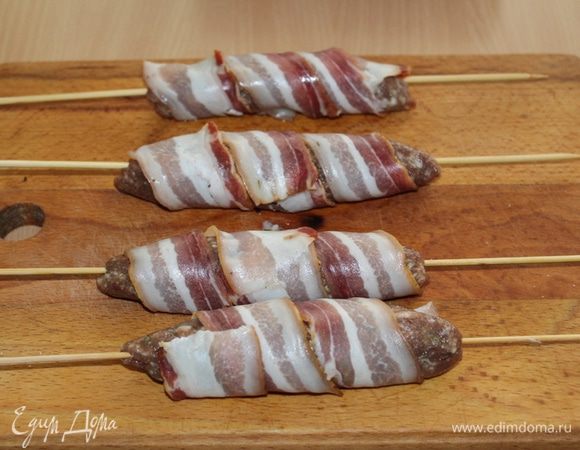 Обернуть колбаски полосками бекона, аккуратно прижав к мясу.