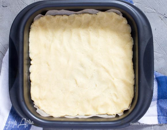 Дно формы для выпечки (22x22 см) застелить пергаментной бумагой и равномерно распределить в ней тесто. 