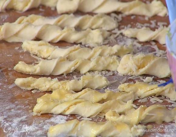 Посыпать тесто оставшимся пармезаном, нарезать длинными тонкими полосками, сложить каждую вдоль пополам сыром внутрь и скрутить спиралькой, сверху смазать желтком с молоком.