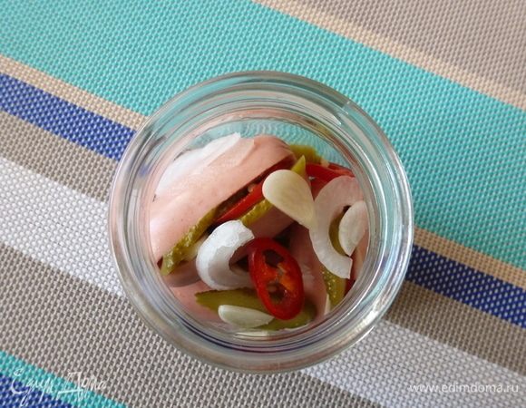 Укладываем сосиски. Переслаиваем их колечками лука, остатками огурца, чеснока и перца.