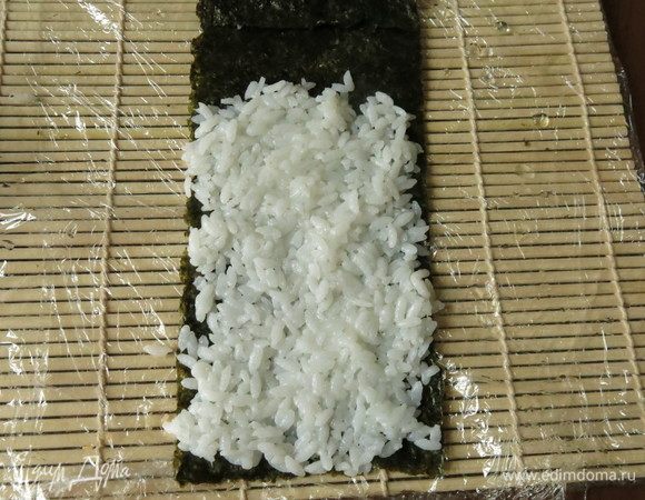 На длинный лист нори выкладываем рис, край листа остается свободным. Рис выкладываем тонким слоем.