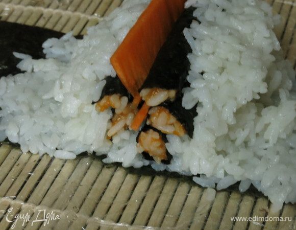 Формируем острые края каждого цилиндра. Выкладываем остальные листики — сперва крупные, по краю чуть меньше, и посередине пластинку тыквы. Закатываем рис с помощью коврика, часть без риса чуть смачиваем и закрепляем.