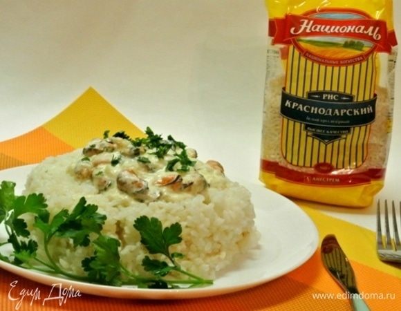 Выложить на тарелку отварной рис, сверху выложить мидии в соусе.