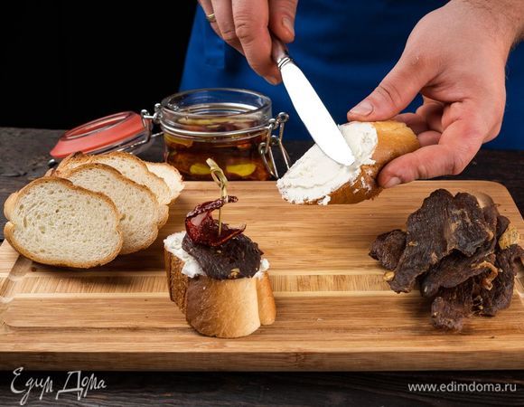 Готовим аппетитную закуску. Нарежьте хлеб небольшими кусочками, намажьте брынзу. На хлеб положите кусочек брынзы, сверху — ароматное джерки, а дальше — вяленый томат.