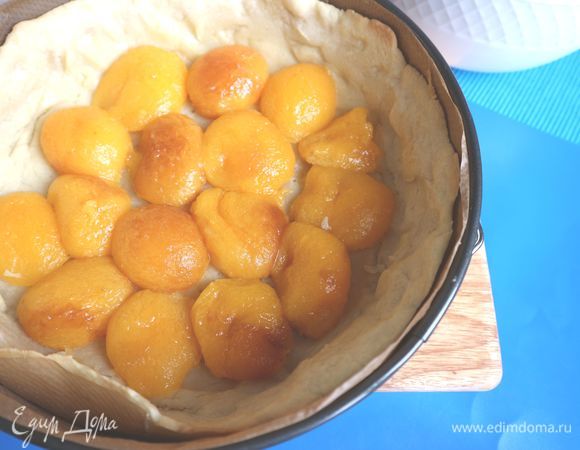 Вынуть форму с тестом из духовки, удалить горох и бумагу, на которой он находился. Дать постоять пару минут. Поместить на тесто абрикосы.