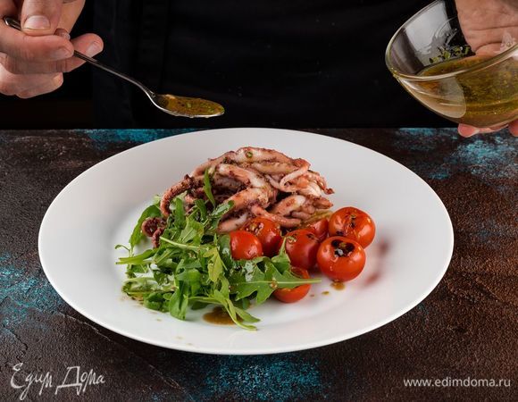 Выложите на широкую тарелку руколу, щупальца кальмара и помидоры черри. Полейте все заправкой.