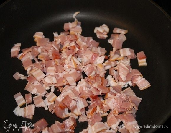 Бекон нарезать мелкими кубиками, обжарить на сухой сковороде до золотистого цвета. Выложить на тарелку и добавить мелко рубленый маринованный огурец.
