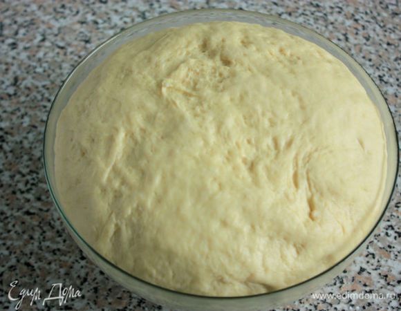 Разогреть духовку до 180°С. Глубокий противень смазать маслом или застелить пекарской бумагой. Подошедшее тесто разделить на 2 части. Поочередно из каждой сделать продолговатый толстый валик, нарезать его на равные кусочки.