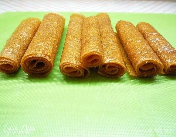 Готовую пастилу переворачиваем бумагой вверх, бумагу смачиваем водой, оставляем на 5-7 минут, затем остатки воды убираем бумажным полотенцем. После этого аккуратно снимаем пергамент. Далее пастилу нарезаем широкими полосками и сворачиваем рулетиками. У меня получилось 300 г пастилы.