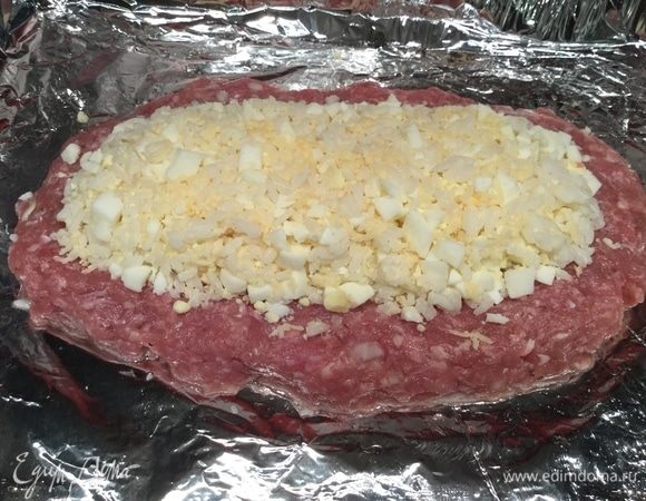 Выложите начинку и сверху оставшийся фарш. Смажьте желтком и выпекайте в духовке 25 минут.