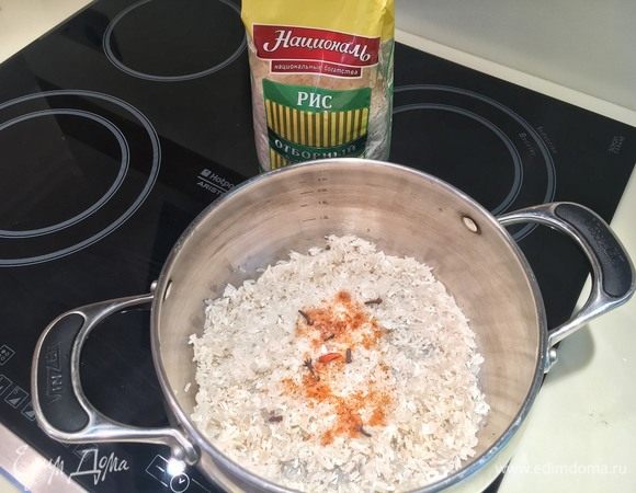 Рис Отборный ТМ «Националь» хорошо промойте холодной водой. Даже если на упаковке написано, что он промытый, не пренебрегайте этим шагом. Вода вымоет из крупы излишек крахмала, и готовый рис будет рассыпчатым снаружи, но слегка клейким внутри. Высыпьте промытый рис в кастрюлю. Добавьте гвоздику, паприку, чили и соль. (Если у вас большой стручок чили, а не птичий глаз, как у меня, то хватит и половины стручка). Залейте холодной водой в соотношении 1:1,5 и накройте крышкой, поставьте на плиту на самый сильный огонь. Максимально быстро доведите до кипения и убавьте огонь до минимума. Пропаривайте рис на маленьком огне 8-10 минут, не поднимая крышки. 
