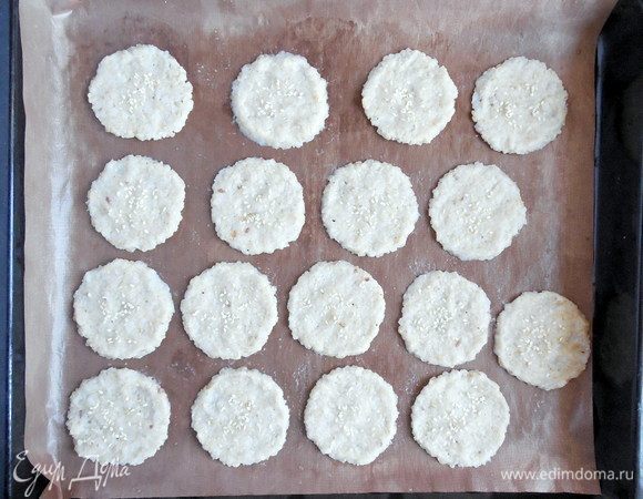 Влажными руками аккуратно расплющить каждый шарик теста в круг диаметром 5-6 см. Посыпать кунжутом. Выпекать 35 мин., пока крекеры не подсохнут и не станут слегка коричневыми. 