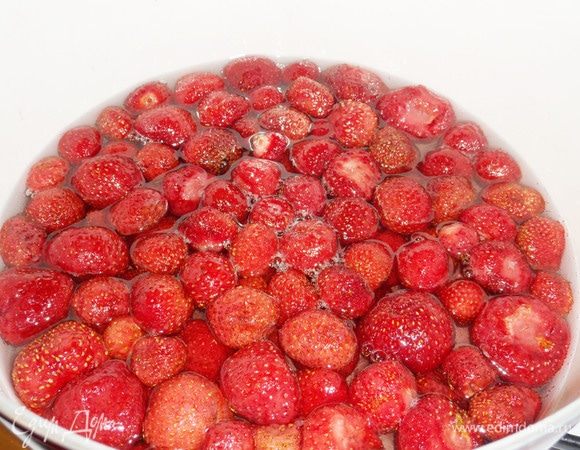 Оставшийся сахар смешать с водой. Поставить на огонь, как только сахарный песок полностью растворится, опустить ягоды клубники в сироп. Варить на слабом огне (сироп должен «шептать») около 10 минут. 